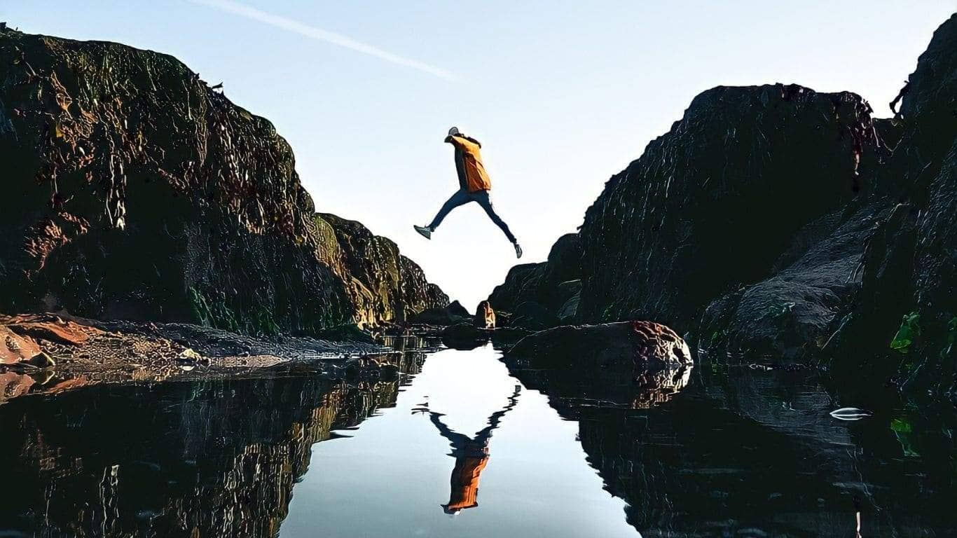 Imagem de uma pessoa saltando,dando a impressão de salta entre as margens de um largio rio